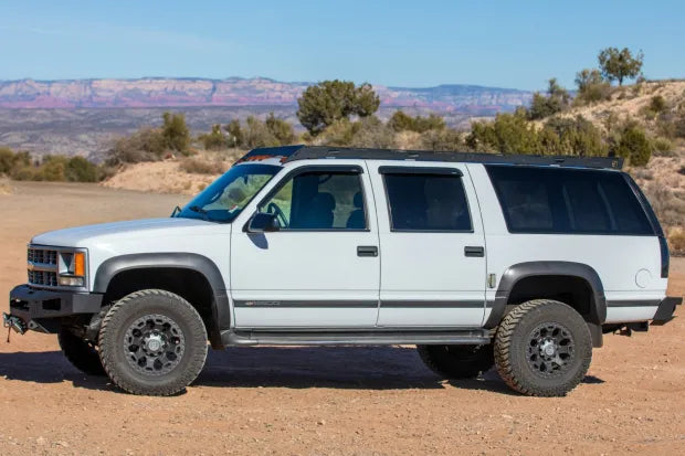 1992-1999 Chevrolet Suburban with roof rack  and Winch Bumper from Baseline Overland. side view white suburban with black rims and 33s